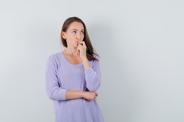 Young woman thinking in lilac blouse and looking focused 