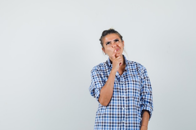 Young woman thinking something while souring her face in checkered shirt and looking focused.