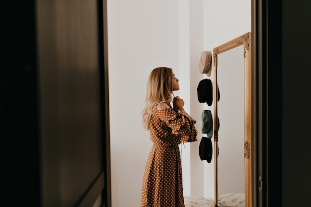 Foto gratuita i legami della giovane donna si inchinano sul suo vestito alla moda. la ragazza si guarda allo specchio prima di andare ad un appuntamento romantico.