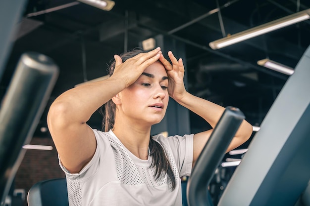 Free photo a young woman tired after intense workout on the exercise bike at the gym