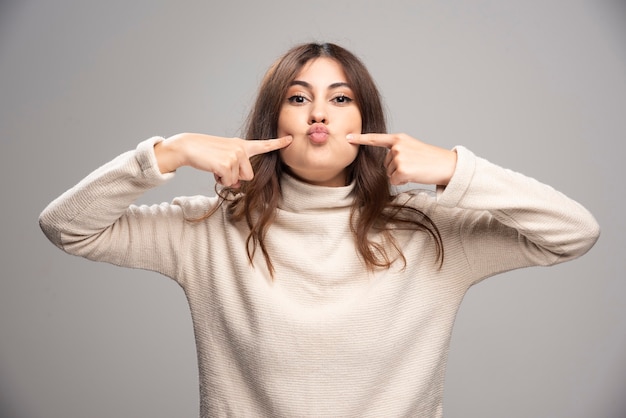 Young woman touching both cheeks with index fingers.