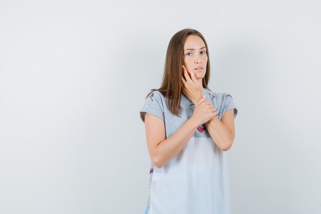Молодая женщина трогательно щеки пальцами в футболке и серьезный вид спереди.