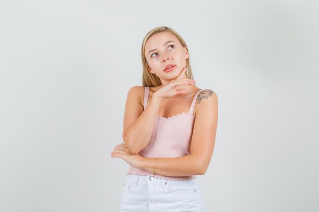 Young woman touching chin with finger while thinking in singlet