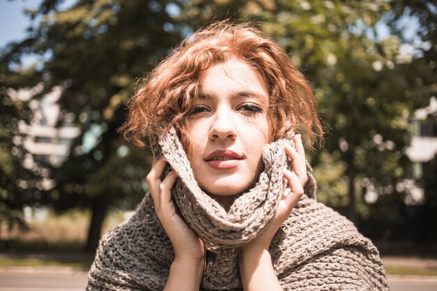 Young woman touching face with scarf in park