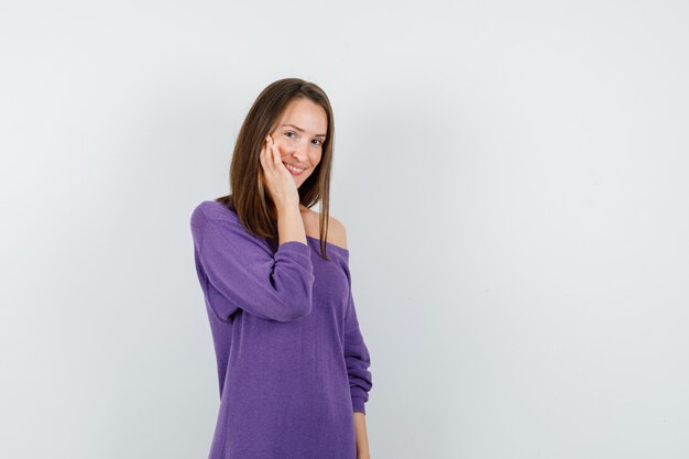 Young woman touching her cheek in violet shirt and looking shy. front view.