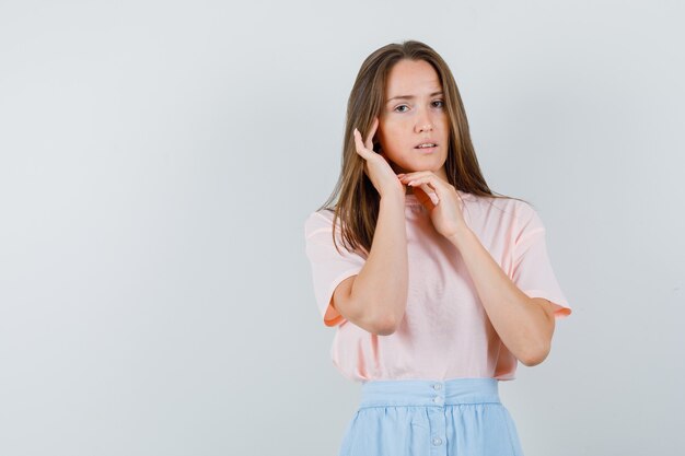 Young woman touching her ear in t-shirt, skirt front view.