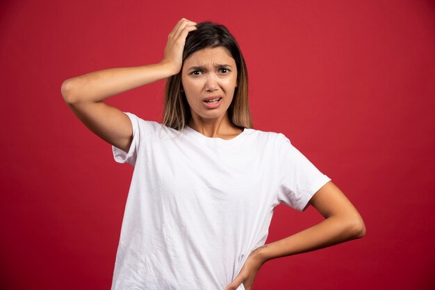 Young woman touching her head on red wall