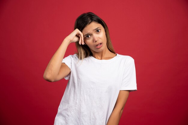 Young woman touching her head on red wall