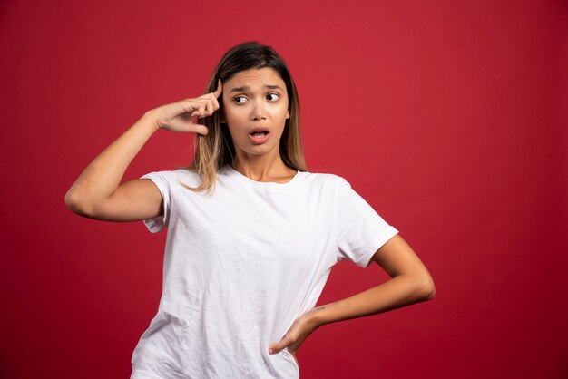 Young woman touching her head on red wall 