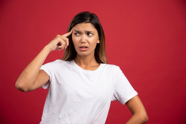 Young woman touching her head on red wall 