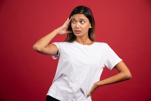 Young woman touching her head on red wall 