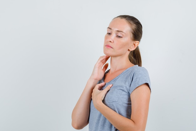 Free photo young woman touching neck with fingers in grey t-shirt , front view.