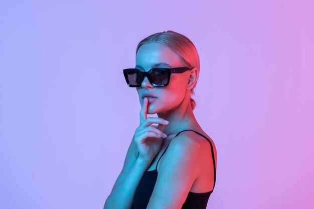 Young woman touching the sunglasses on the pink background.