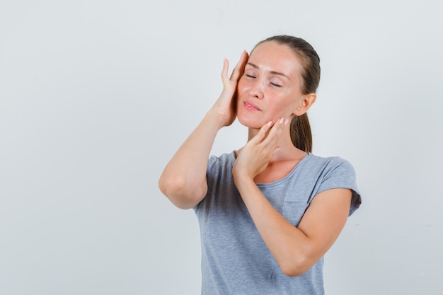 Young woman touching temples with closed eyes in grey t-shirt and looking peaceful , front view.