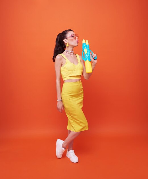 Young woman tourist happy with water gun during Songkran festival holiday on orange background