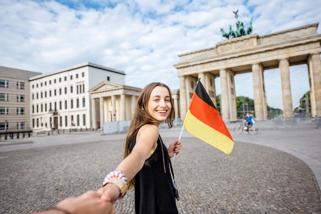 Молодая туристка идет с немецким флагом к знаменитым бранденбургским воротам в берлине. следуй за мной концепция