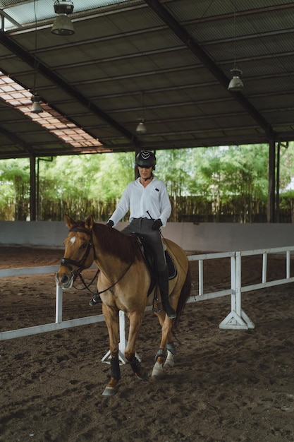 Молодая женщина тренируется в верховой езде на арене. Молодая кавказская женщина в формальной одежде верхом на лошадях по песчаной арене. Породистая лошадь для конного спорта. Спортсменка на лошади