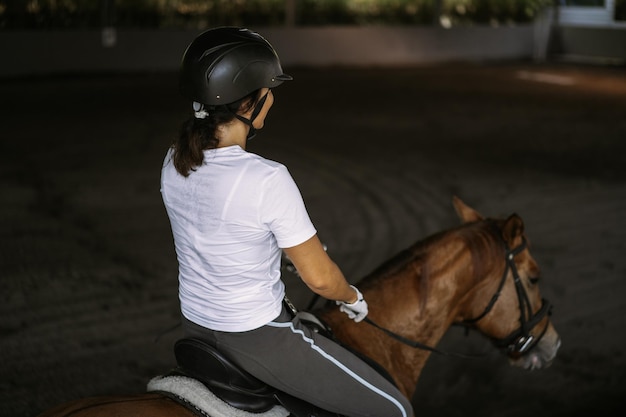 Молодая женщина тренируется в верховой езде на арене. молодая кавказская женщина в формальной одежде верхом на лошадях по песчаной арене. породистая лошадь для конного спорта. спортсменка на лошади