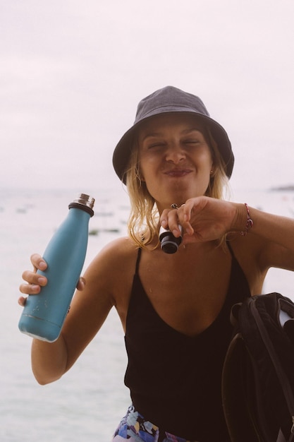 Young woman traveler drinks water from a colored bottle.