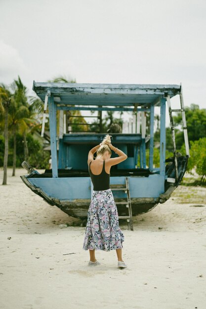 Молодая женщина путешествует по пляжу на фоне старого корабля.