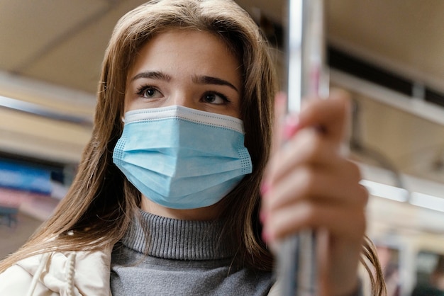 무료 사진 수술 용 마스크를 쓰고 지하철로 여행하는 젊은 여자