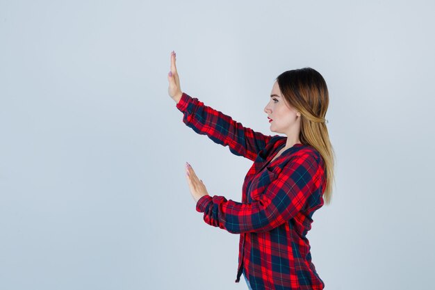 Young woman trying to block herself with hands in checked shirt and looking scared .