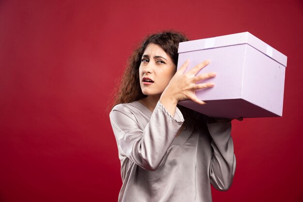 Молодая женщина пытается слушать фиолетовую подарочную коробку.