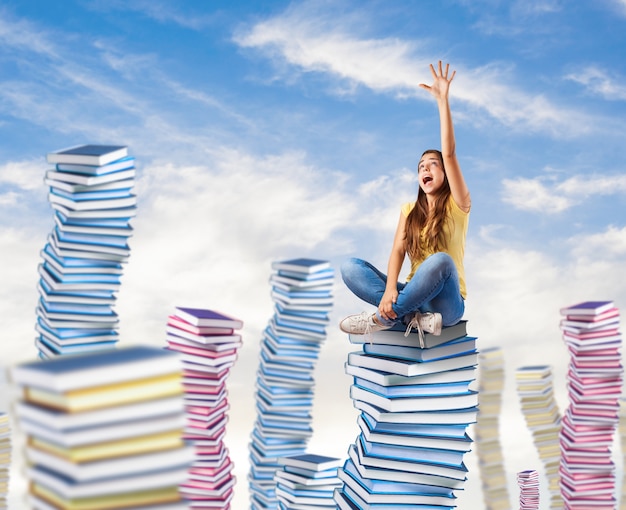 young woman trying to reach something sitting on a books tower