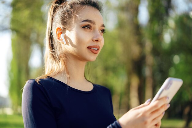 若い女性は、屋外でスマートフォンで実行するために音楽をオンにします