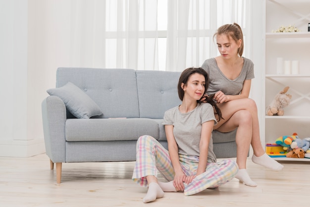 Young woman tying the braids of her girlfriend at home