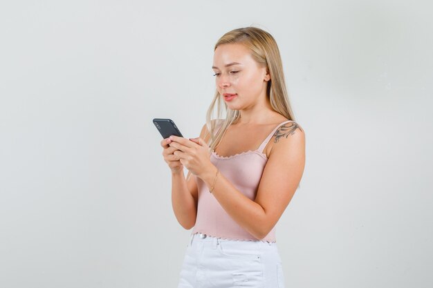 Young woman typing on smartphone and smiling in singlet