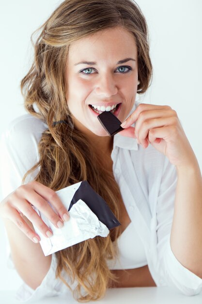 초콜릿을 먹는 속옷에 젊은 여자. 흰색에 격리.