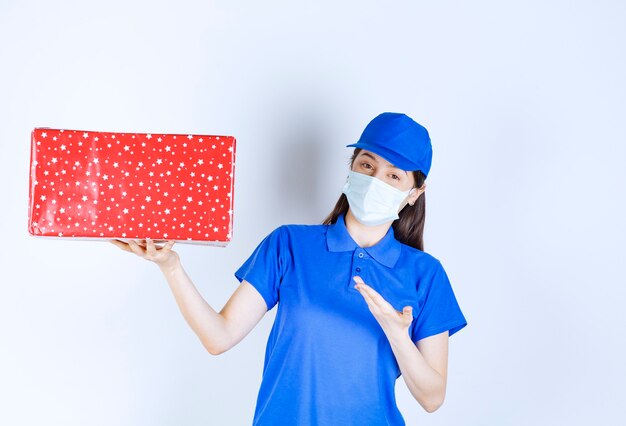 Young woman in uniform and medical mask holding Christmas present . 