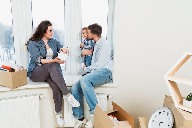 Free photo young woman unpacking the cardboard boxes looking at his husband loving his son