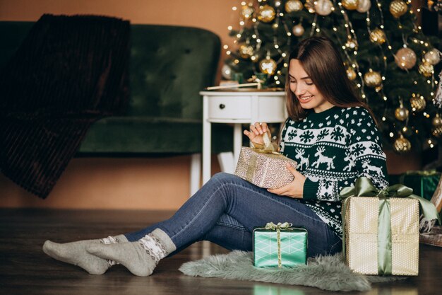 クリスマスツリーでクリスマスプレゼントを開梱する若い女性