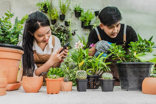 若い女性はスマートフォンを使用してサボテンの写真を撮り、彼女は幸せに微笑む、若い男性は観葉植物の世話をします
