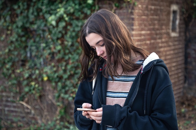 A young woman uses a phone on the background of a wall with ivy