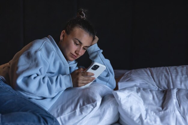 한 젊은 여성이 저녁에 침대에 누워 스마트폰을 사용한다