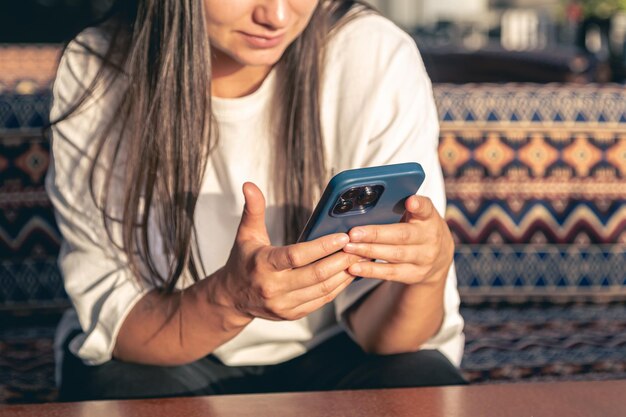 Foto gratuita una giovane donna usa uno smartphone mentre è seduta in un bar all'aperto al tramonto