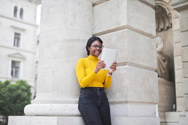 young woman uses tablet leaning against a school wall