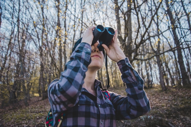 Free photo young woman using binoculars in the forest