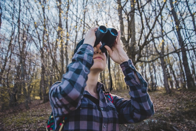 Young woman using binoculars in the forest