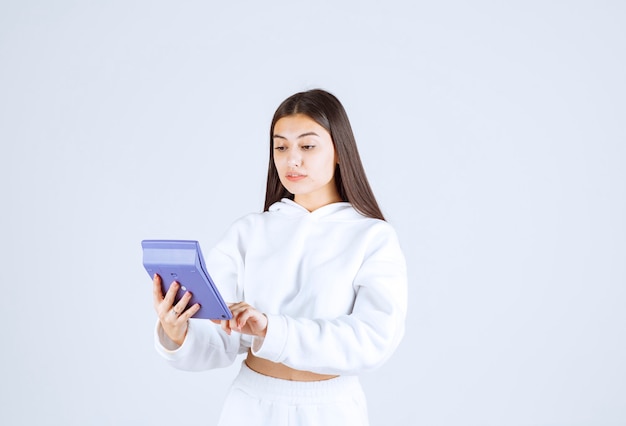 young woman using a calculator on white-gray background.