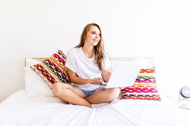 Free photo young woman using laptop on bed. woman working on laptop in bed at home