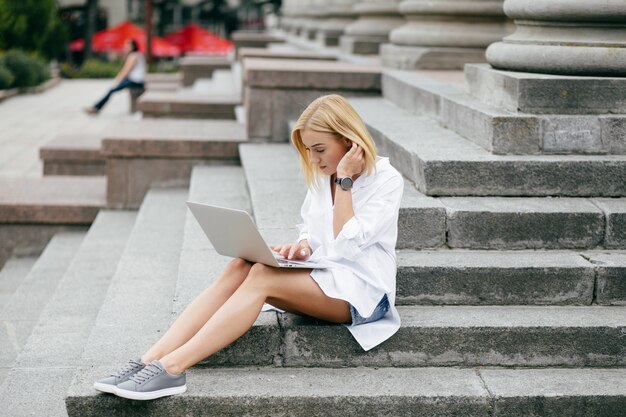Молодая женщина, используя портативный компьютер и смартфон. Красивая студент девушка, работающих на ноутбуке на открытом воздухе