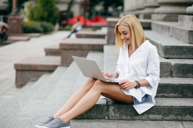 랩톱 컴퓨터와 스마트 폰을 사용하는 젊은 여자. 야외 노트북에서 일하는 아름 다운 학생 소녀