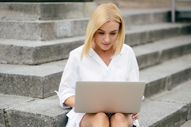 ラップトップコンピュータとスマートフォンを使用している若い女性。ラップトップの屋外で働く美しい学生少女