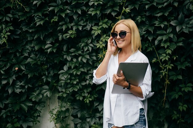 Giovane donna con computer portatile e smart phone. bella ragazza studente che lavora al computer portatile all'aperto