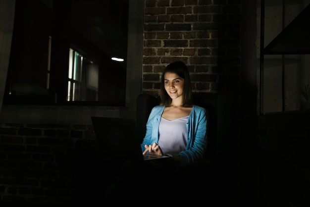 Молодая женщина, используя ноутбук в темной комнате