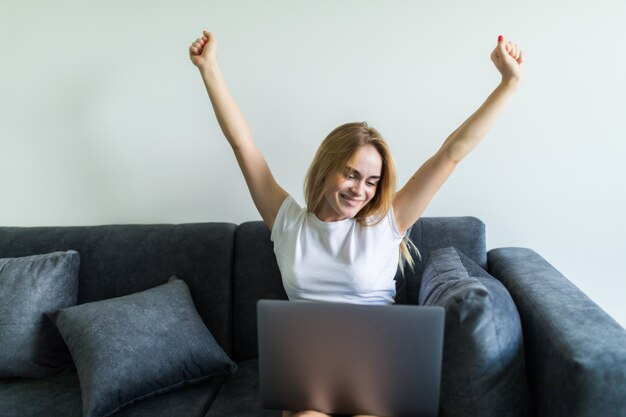 Young woman using a laptop while raising hand and sitting on the couch at home